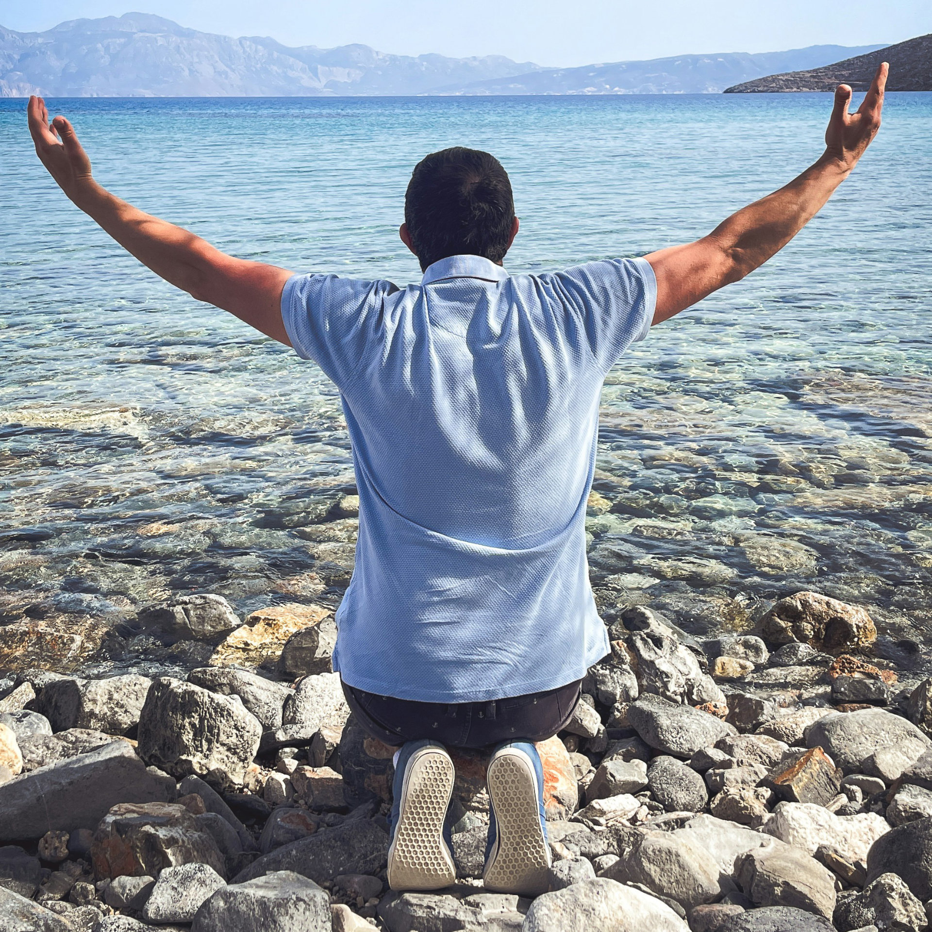 Uomo inginocchiato con le braccia alzate verso il mare