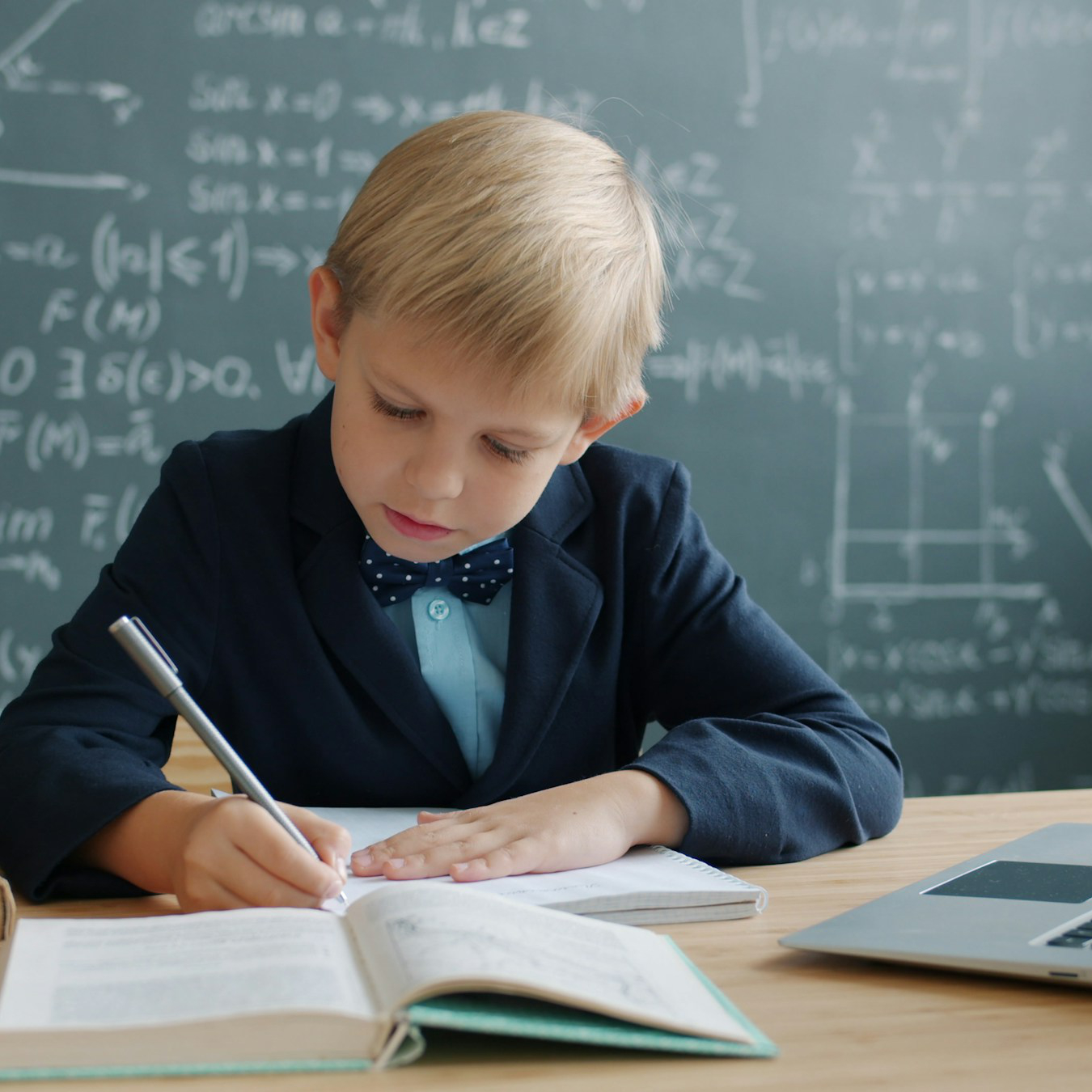 Giovane ragazzo in giacca e cravatta che scrive a una scrivania